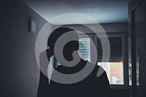 Silhouette of depressed sad man in dark room with window shutters pulled down