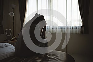 Silhouette depressed woman sadly sitting on the bed in the bedroom. Sad asian women suffering depression insomnia awake and sit