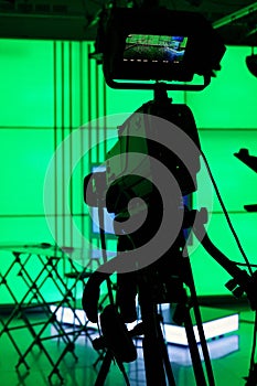 Silhouette of a digital video camera in front of a green screen.