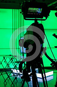 Silhouette of a digital video camera in front of a green screen.