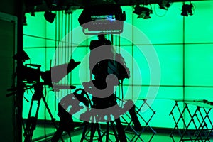 Silhouette of a digital video camera in front of a green screen.