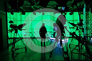 Silhouette of a digital video camera in front of a green screen.