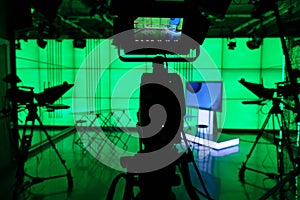Silhouette of a digital video camera in front of a green screen.
