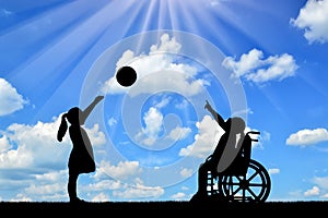 Silhouette of a disabled child girl in a wheelchair and healthy girl playing in a ball outdoors photo