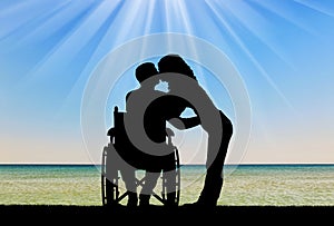 Silhouette of a disabled man in a wheelchair and his wife who is kissing by the sea