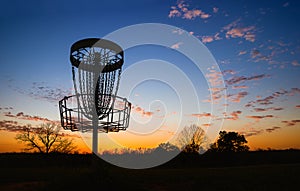 Silhouette of disc golf basket against sunset photo
