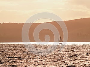 Silhouette distant hills and yacht sailing in under red sky at sunset