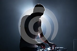 Silhouette of a DJ performing on party in night club. Cool young man playing music on stage