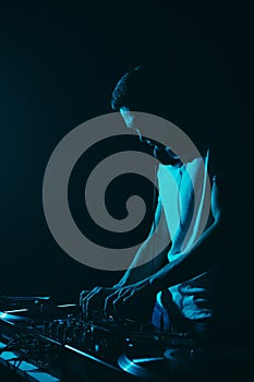 Silhouette of a DJ playing techno music in blue stage lights. Club disc jockey performing on stage in the dark