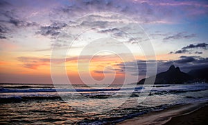 Silhouette of Dois Irmaos Mountain, beautiful sky of sunset and reflection of the sky in Atlantic ocean at Ipanema beach