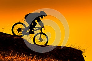 Silhouette of downhill mountain bike rider at sunset