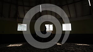 Silhouette of dressage rider walking horse through stables. Slow motion