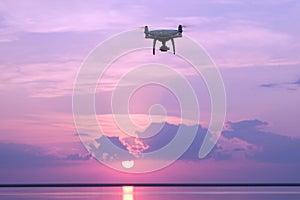 Silhouette of a drone at sunrise over the lake against the sky with the rising sun. Quadcopter, clouds, morning sunlight. Aerial p