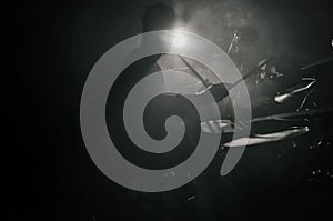 The silhouette of a drummer playing a drum kit on stage in the rays of light from spotlights