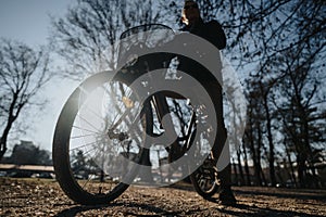 Silhouette of an elderly man leisurely cycling on a pathway in a park, with sunlight filtering through the bicycle wheel