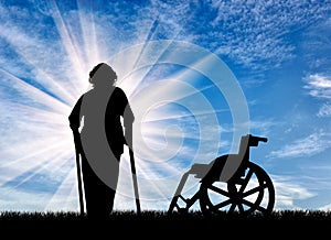 Silhouette of an elderly woman with crutches on background of wheelchair outdoors