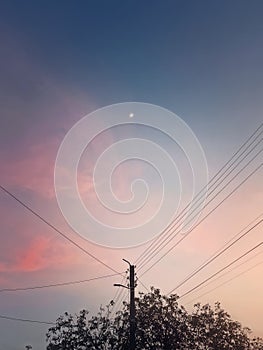 Silhouette of electric pillar with cables over purple sunset sky background with the moon shining in the sky above