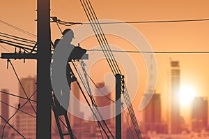 Silhouette electrician is installing cable lines to connecting internet signal on electric power pole in sunset time