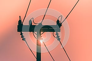 Silhouette of electricity pole and high voltage power line with sunset in the background.