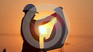 Silhouette of an engineer looks at the project of construction of a high-voltage power plant. The engineer is reading