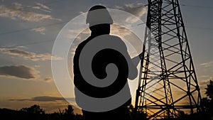 Silhouette of engineer standing on field with electricity towers. Electrical engineer with high voltage electricity