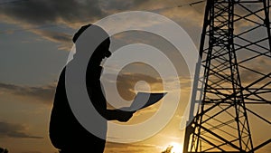 Silhouette of engineer standing on field with electricity towers. Electrical engineer with high voltage electricity