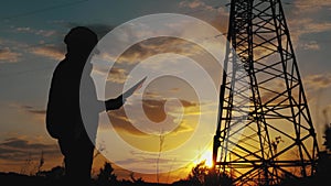 Silhouette of engineer standing on field with electricity towers. Electrical engineer with high voltage electricity