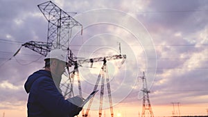 Silhouette of engineer standing on field with electricity towers. Electrical engineer with high voltage electricity