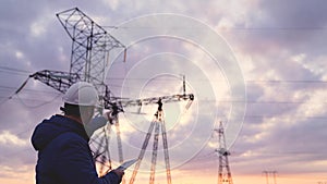 Silhouette of engineer standing on field with electricity towers. Electrical engineer with high voltage electricity