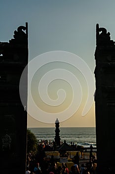 Silhouette of entrance gate at Tanah Lot temple with crowd of people enjoying sunset in background