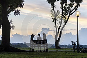 Silhouette of family enjoying sunset at park with bicycle parked beside lamp post.