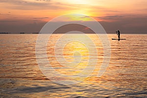 Silhouette of family playing the stand-up paddle board on the sea with beautiful summer sunset colors. Happy family concept