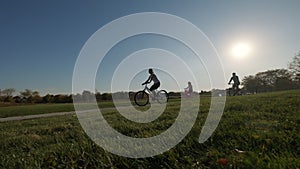 Silhouette of a family riding bicycles in a park and on a suburban street on a sunny day. Wide shot footage. Slow motion