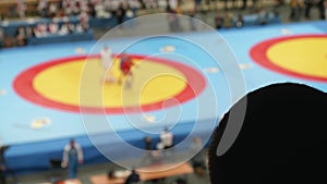 Silhouette of fan who watches duelling on sambo. The action is unfocused. Fan is unrecognizable.