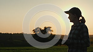 The silhouette of a farmer walks along a wheat field with a tablet in his hand