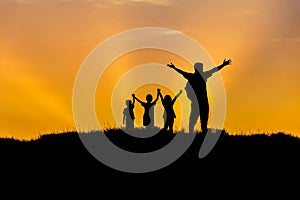 Silhouette father and children standing raised hands up on sunset