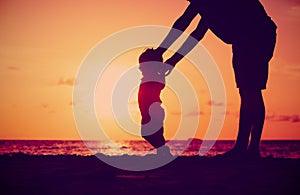 Silhouette of father and daughter learning to walk at sunset