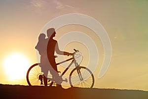 Silhouette of father and little daughter biking at sunset