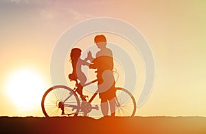 Silhouette of father and little daughter biking at sunset