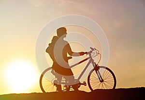 Silhouette of father and little daughter biking at sunset