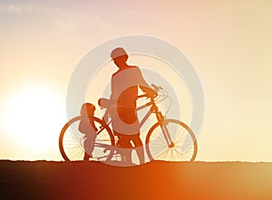 Silhouette of father and little daughter biking at sunset