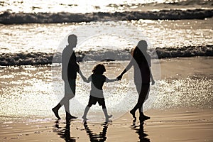 Silhouette of father, mother and child son holding hands and walking on beach.