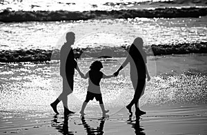 Silhouette of father, mother and child son holding hands and walking on beach.