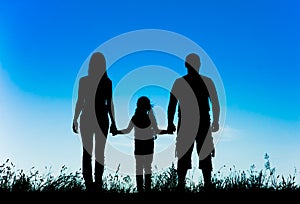 Silhouette father, mother and daughter holding hands at sunset