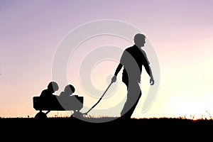 Silhouette of Father Pulling Sons in Wagon at Sunset