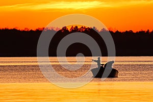Silhouette of father and son fishing on lake at sunset.