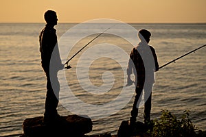 Silhouette of father and son fishing at sunset in summer on the sea