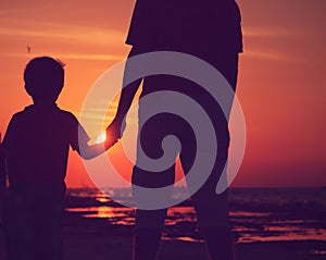 Silhouette of father and son holding hands at sunset sea