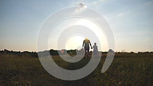 Silhouette of father and son walking on the field at sunset and holding hands of each other. Happy family spending time