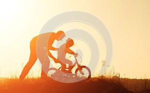 Silhouette of father teaching his daughter to ride a bike at sunset